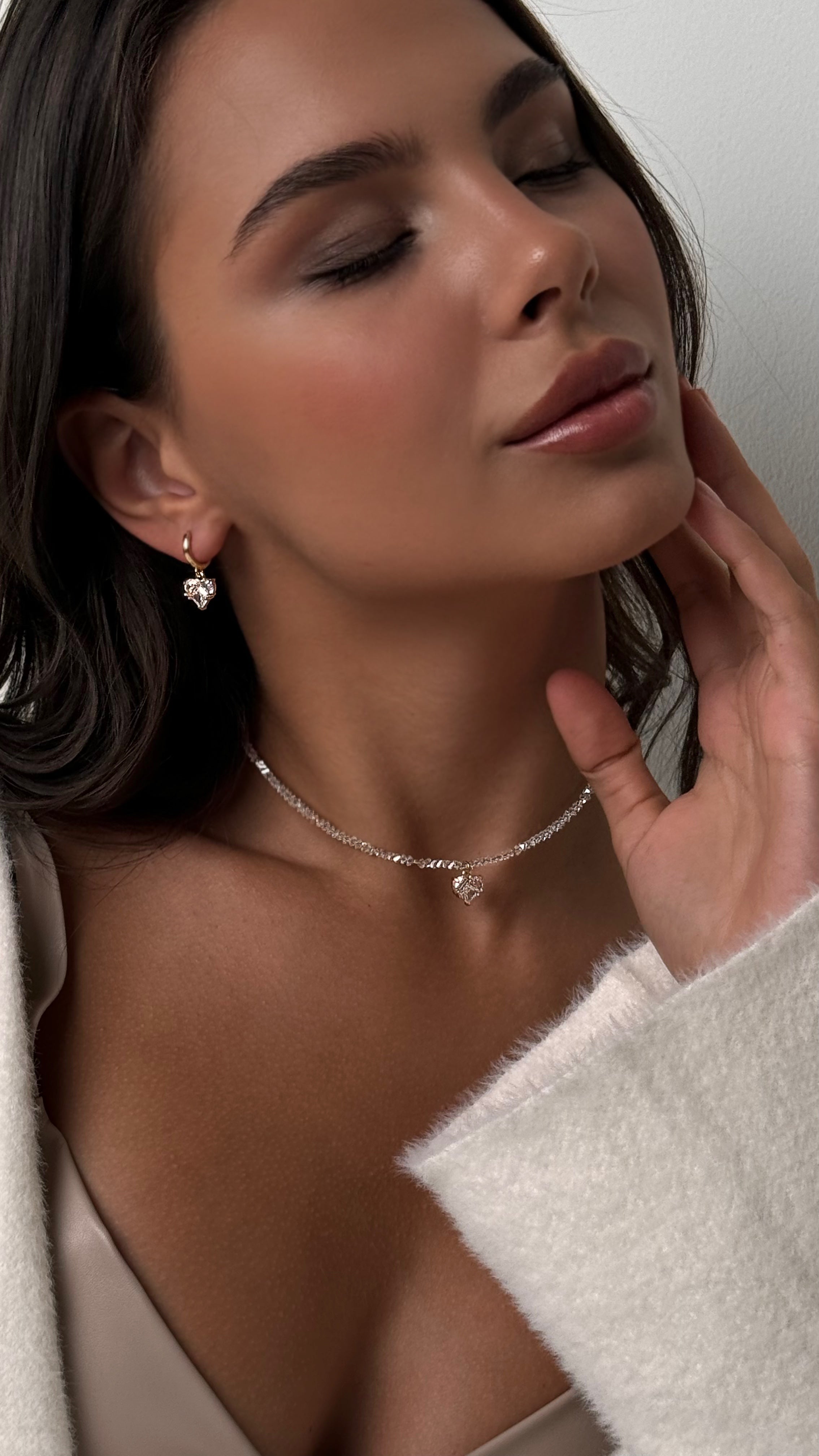 Woman wearing a necklace and earrings, with a hand touching her ear.