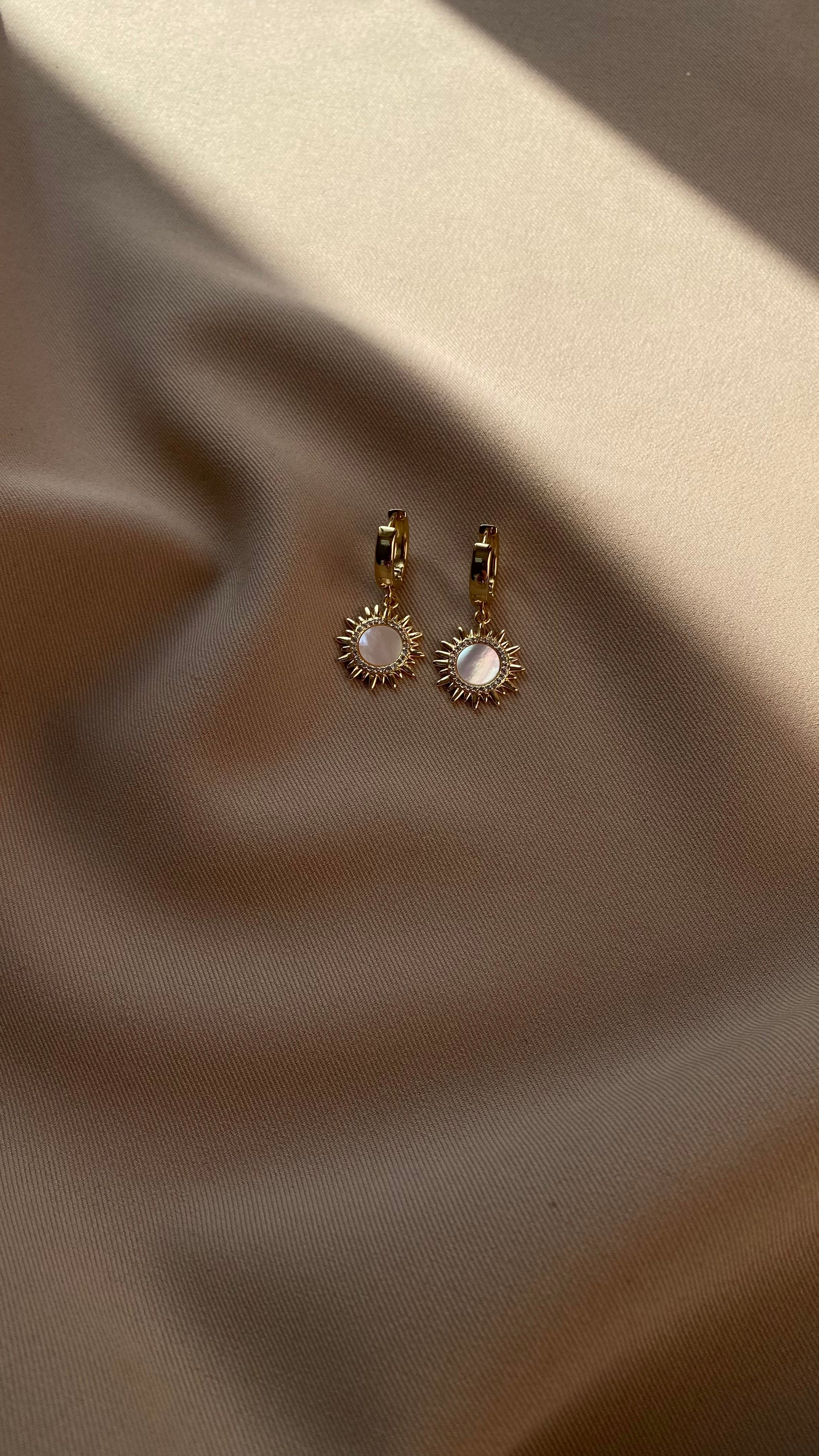 Gold-plated hoop earrings with a central gemstone on a beige fabric background