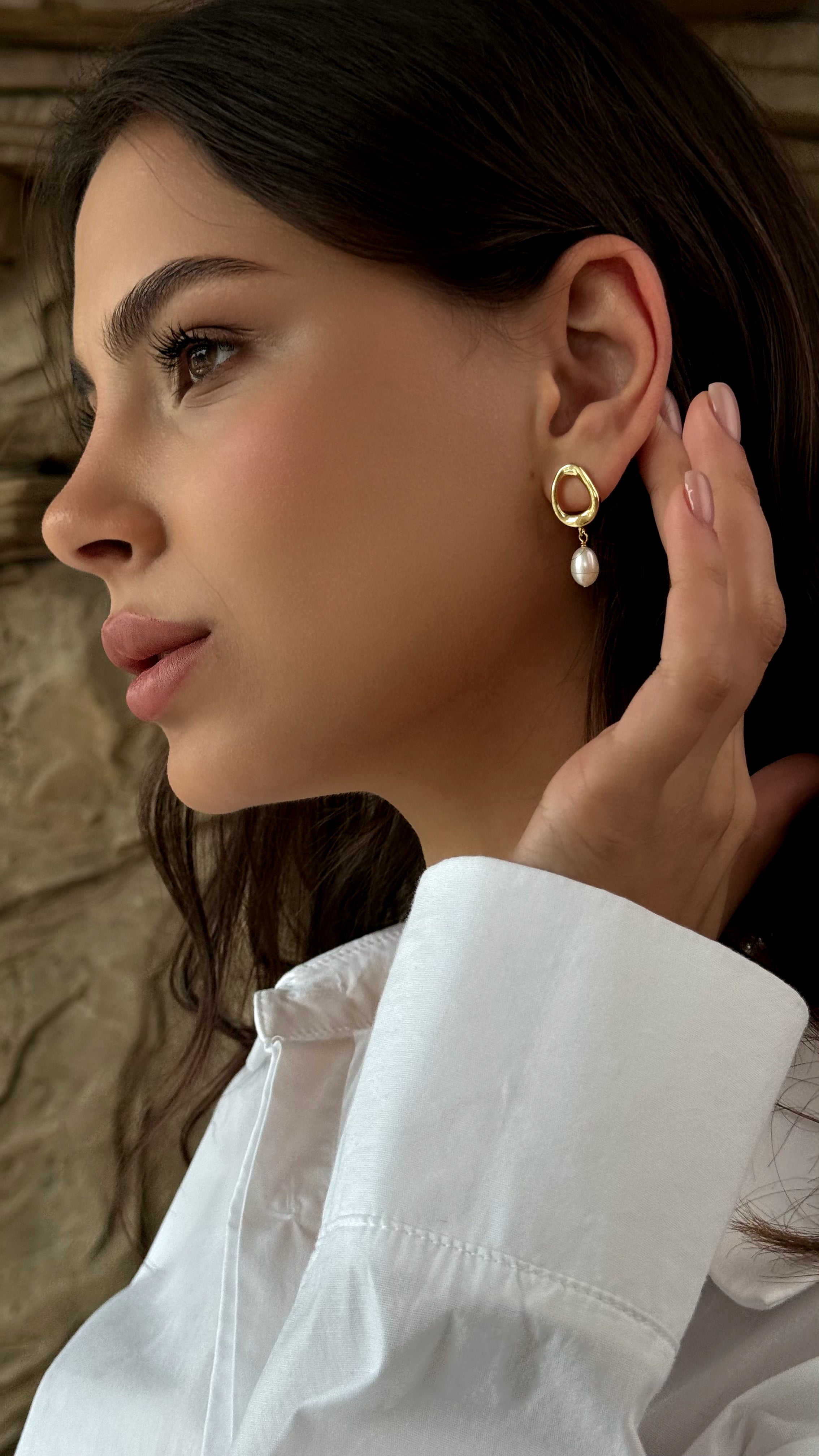 Woman wearing gold-plated earrings with a pearl drop, against a neutral background