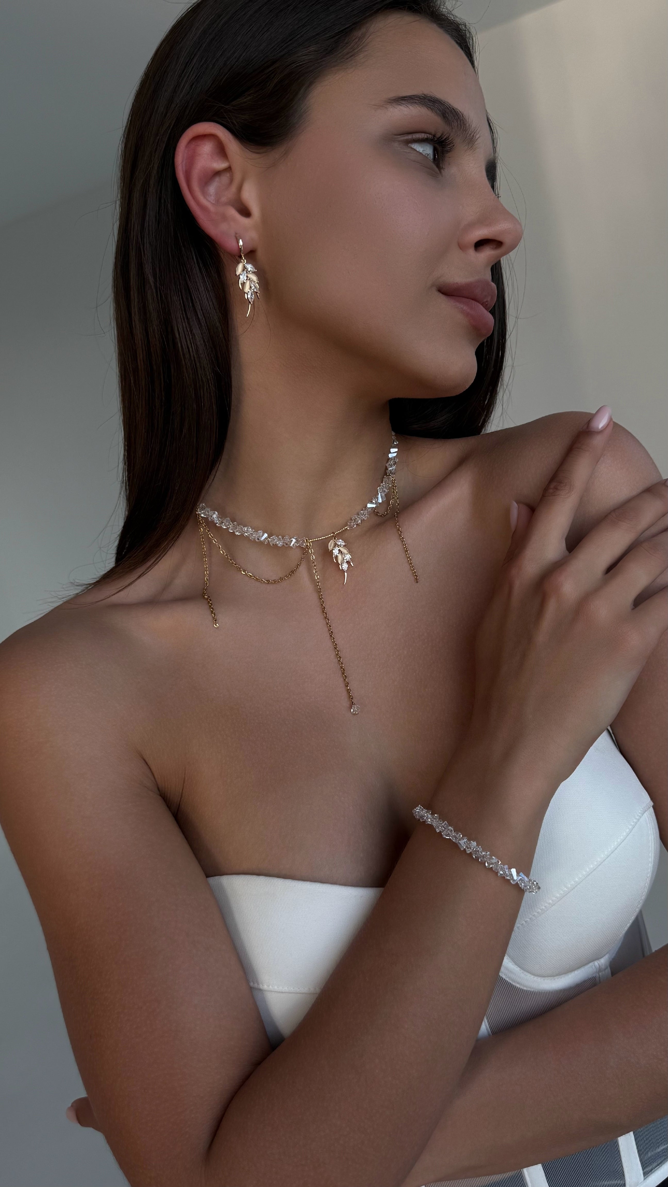 Woman wearing gold-plated necklaces, bracelet and earrings with a neutral background