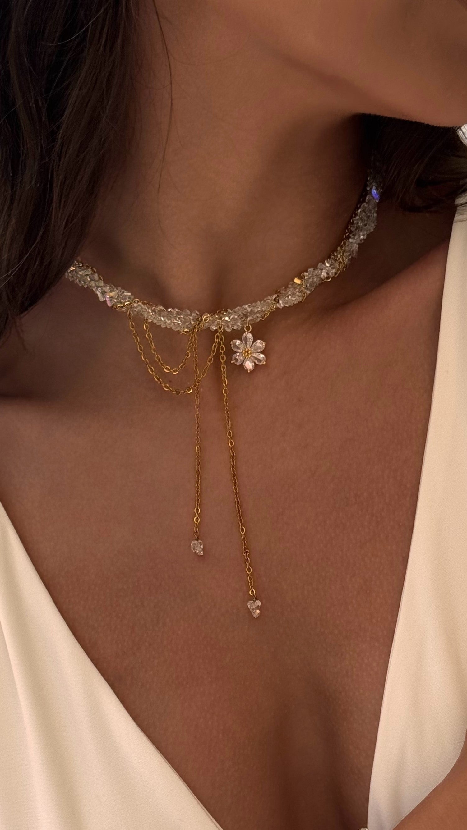 Close-up of a delicate gold-plated necklace with floral pendant on a person wearing a white top.