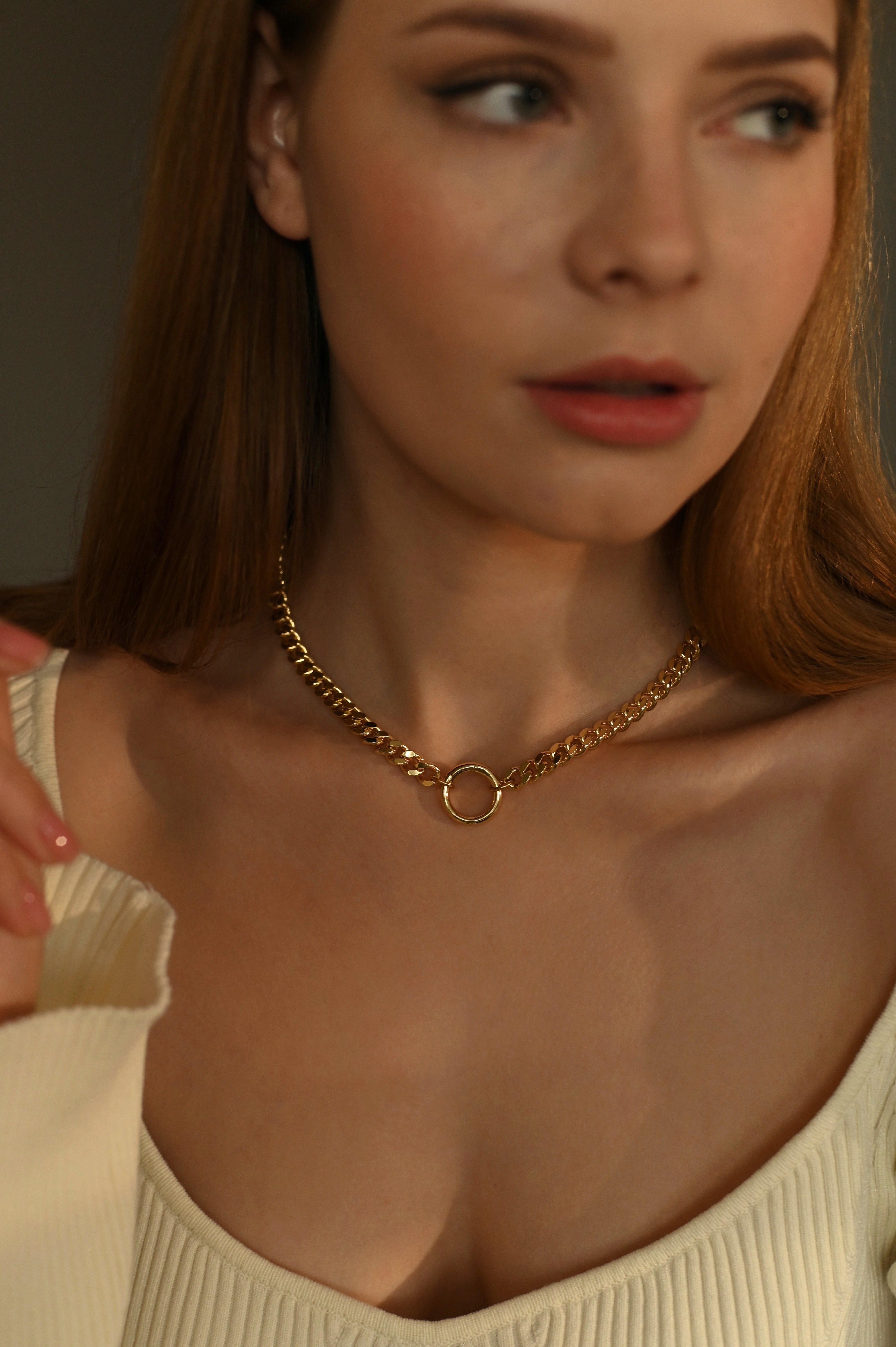 Woman wearing a gold-plated chain necklace with a neutral background