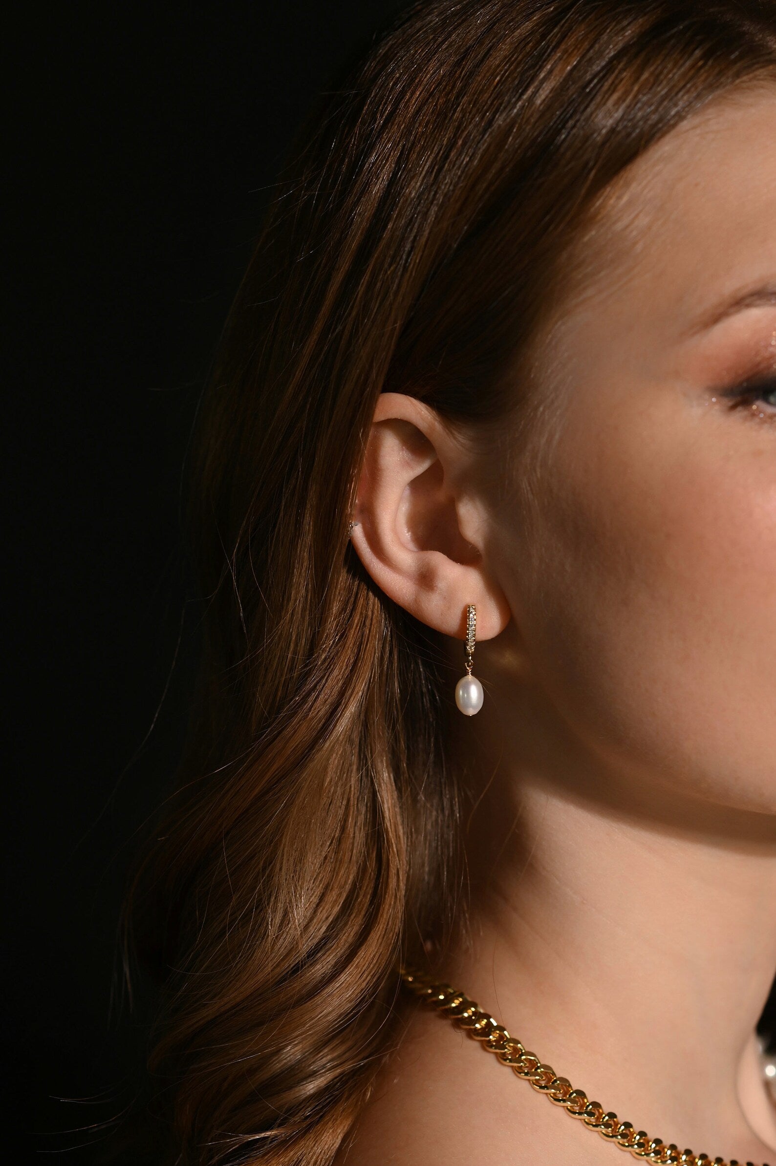 Close-up of a woman wearing pearl earrings with a dark background
