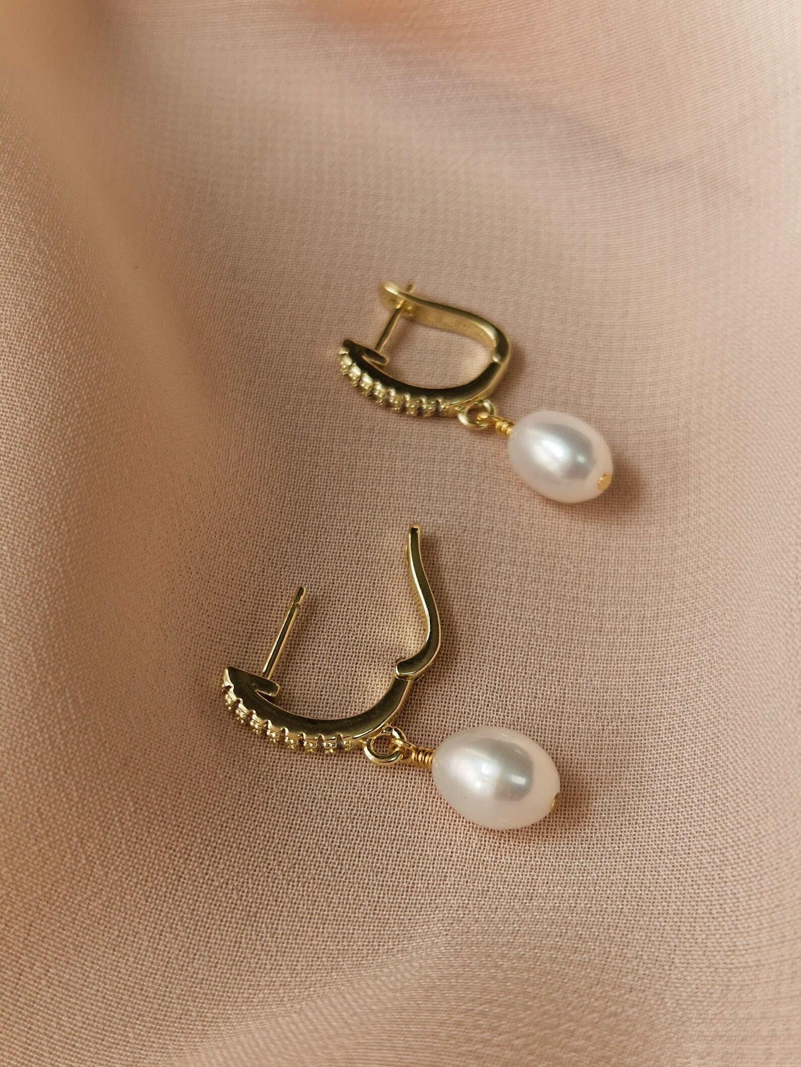 Gold-plated earrings with pearl drops on a beige fabric background