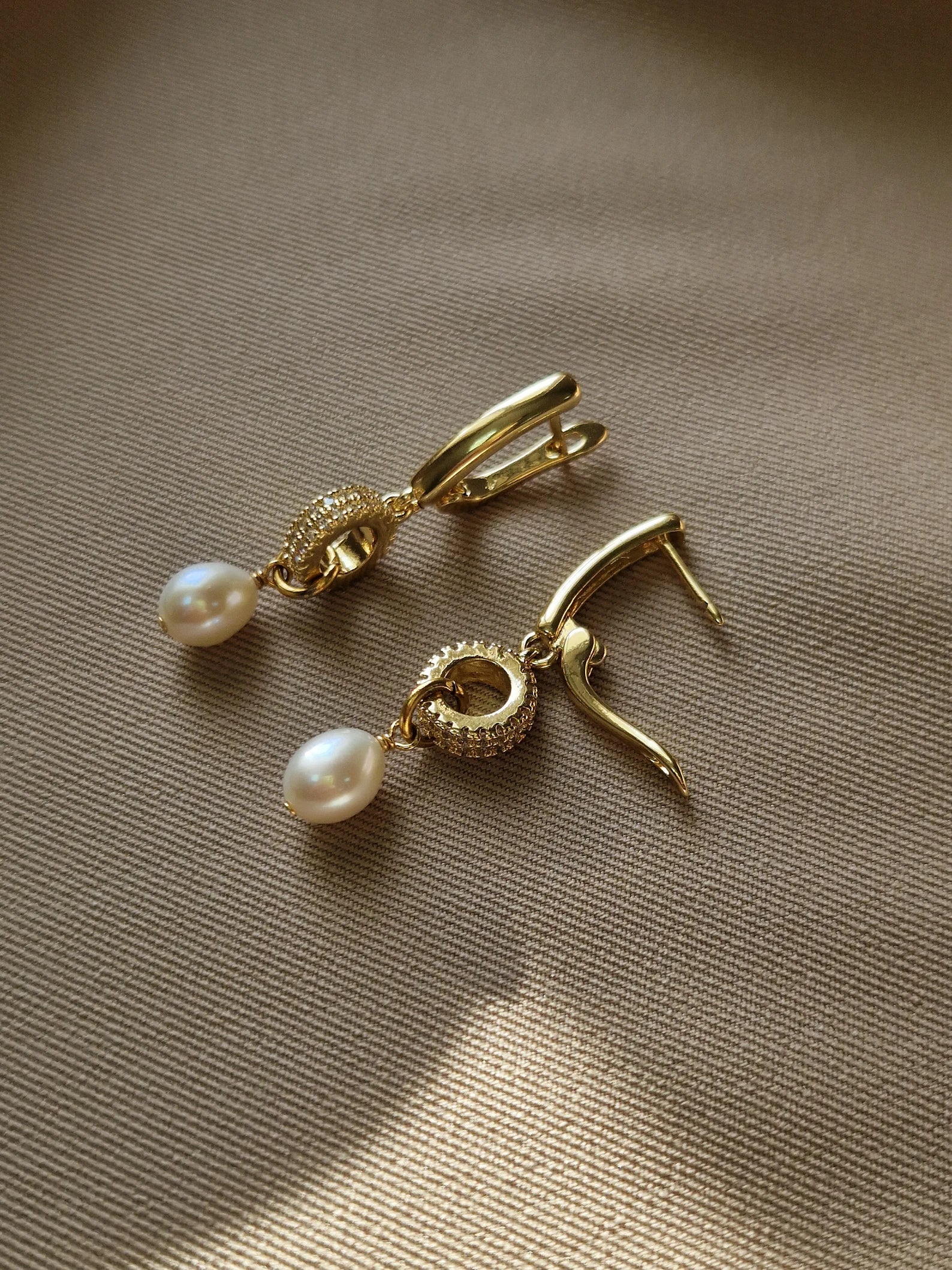 Gold-plated earrings with pearl drops on a beige fabric backgroundted