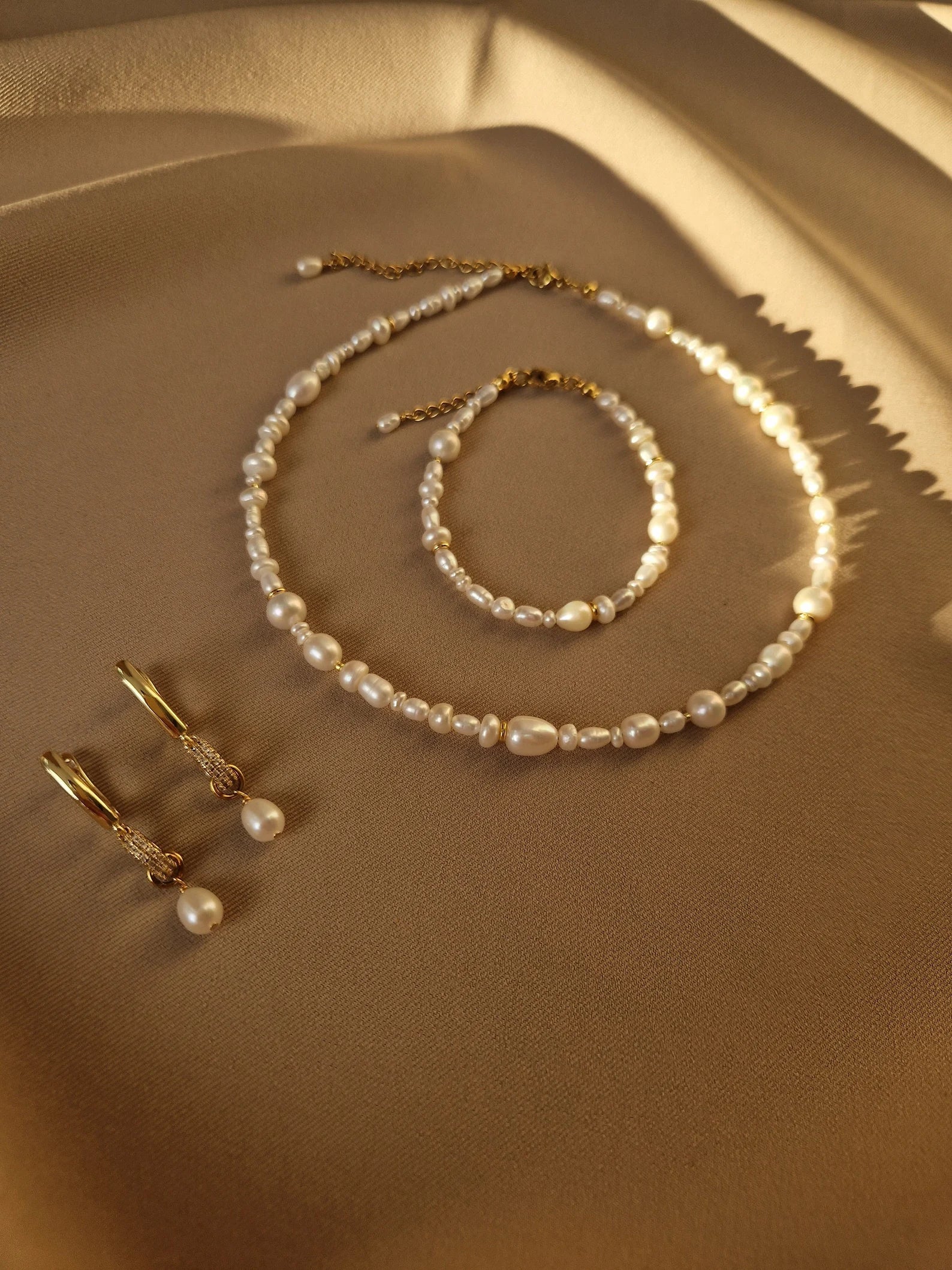 Pearl necklace, bracelet, and earrings on a beige surface